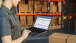 © Gorodenkoff - Female Manager Using Laptop Computer To Check Inventory. In the Background Warehouse Retail Center with Cardboard boxes, e-Commerce Online Orders, Food, Medicine, Products Supply. Over the Shoulder