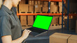 Female Manager Using Green Screen Chroma Key Laptop. In the Background Warehouse Retail Center with Cardboard boxes, e-Commerce Online Orders, Food, Medicine, Products Supply. Over the Shoulder