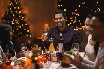 Wall Mural - holidays, party and celebration concept - multiethnic group of happy friends having christmas dinner at home and drinking wine