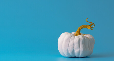 white pumpkin with golden shiny stem on a blue background, minimalism concept Halloween