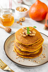Wall Mural - Pumpkin pancakes in a ceramic plate on a light gray culinary background close-up