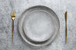 Elegance empty table setting with empty gray plate with golden cutlery as mockup on grey stone background. Top view.