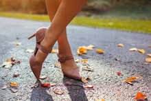 Close Up Of Female Shoes. Woman Wears Stylish Brown High-heeled Shoes In Autumn Park Standing Among Falling Leaves.