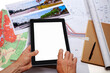 Urbanisme - Aménagement du territoire - technicien tenant une tablette numérique, au dessus de cartes de plan de masse d'un projet de voirie et giratoire posés sur un bureau