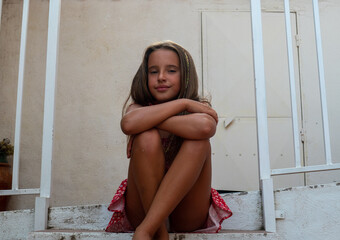 cute teenage caucasian smiling girl with long hair sitting on the stairs with legs and arms crossed