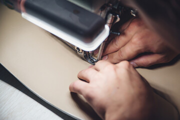 Wall Mural - Working process of leather craftsman. Tanner sews leather on a special sewing machine, close up.