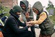 © pressmaster - Positive young Black man in hat playing with kids against abandoned building and hanging clothes on rope in refugee camp