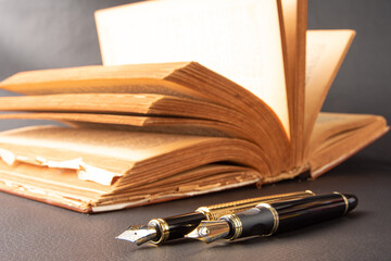 Fountain pen, beautiful details of two beautiful fountain pens and an antique book placed on black leather, selective focus.