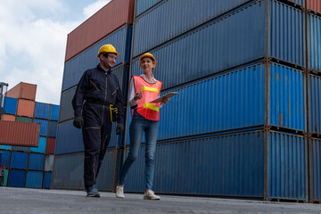 Industrial worker works with co-worker at overseas shipping container yard . Logistics supply chain management and international goods export concept .