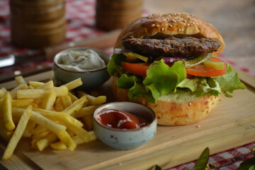 Poster - Closeup of a delicious burger with french fries and sauces on a board in a restaurant