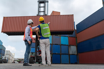 Industrial worker works with co-worker at overseas shipping container yard . Logistics supply chain management and international goods export concept .