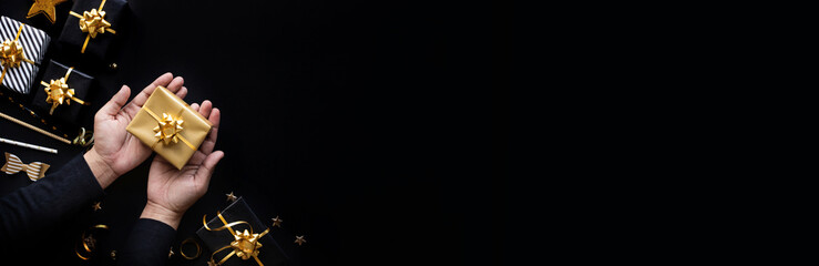 Wall Mural - party and celebration with person hand giving golden gift box on dark color background