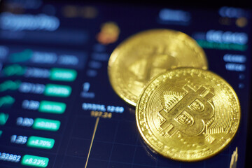 Two gold bitcoin coins lie on the tablet screen, which shows indicators of changes in cryptocurrency rates