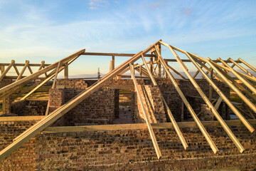 Wall Mural - Private residential house with wooden roof frame structure under construction. Unfinished brick building under development.