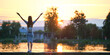© bilanol - Back view of lonely woman standing on lake side with outstretched hands on warm summer evening. Success and vitality concept.