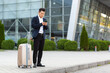© Liubomir - Businessman trying to call a taxi using an app and a mobile phone, asian man at the train station with a big suitcase