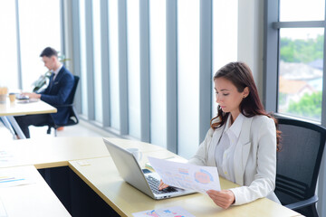 Portrait of Concentrated and confidence businesswoman is working. She holding a paperwork and using laptop on desk. Start-up modern office or workplace background.