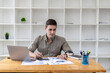 © kamiphotos - Young businessman sitting and checking financial documents displayed in chart format, young businessman who founded a startup company, managing a new business to grow by leaps and bounds.