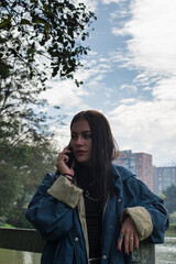 Young caucasian woman dressed in blue talking with her smartphone next to lake in a green park 