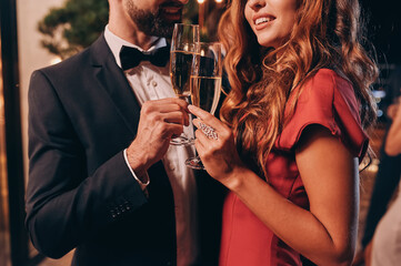 Wall Mural - Close up of beautiful young couple in formalwear toasting with champagne while spending time on luxury party