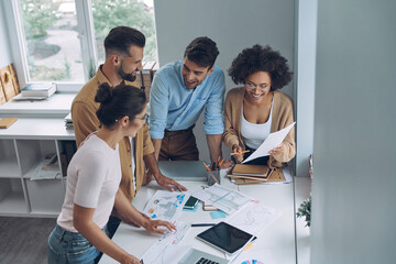 Wall Mural - Top view of confident young business team having quick meeting while standing in office together