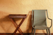 Woven Chairs And A Wooden Table Stand Against A Rugged Concrete Wall Painted In Yellow.