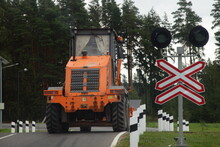 Big Heavy 3-axle Orange Wheeled Bulldozer Tractor Drive On Suburban Highway Railroad Crossing With Sign At Summer Day, Industrial Machine Traffic On The Road