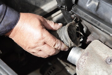 Wall Mural - Turning off the air heating for an automobile engine intake in summer - a man's hand removes the pipe from the exhaust manifold heat shield under hood close up, seasonal vehicle maintenance service