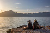 Fototapeta Desenie - Italy - Lake Garda in the town of Torri del Benaco. A sunset, a romantic couple by the water, in the distance you can see the mountain peaks.