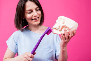 Wall Mural - Beautiful woman brushing teeth of an artificial skull using a large toothbrush