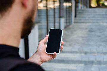 Wall Mural - a man with a smartphone in his hands stands near the business center. a businessman is sending a tex