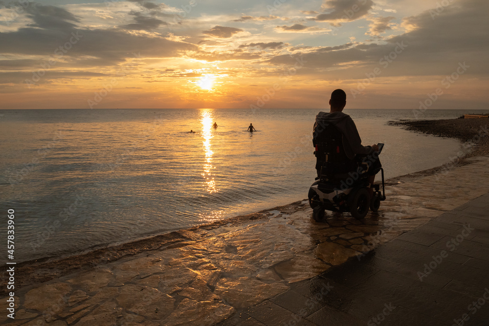 Disabled person in a wheelchair at sunset looking at sea. Stock Photo ...