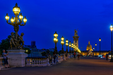 Fototapete - Pont Alexandre III bridge over river Seine and Hotel des Invalides on background at night in Paris, France.  Cityscape of Paris. Architecture and landmarks of Paris.