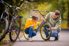 Dad And Daughter Inspect Wheel Of Children's Teenage Bicycle On The Autumn Path Of The Park.
