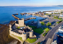 Medieval Norman Castle In Carrickfergus Near Belfast In Sunrise Light. Aerial View With Marina, Yachts, Parking, Town And Far View Of Belfast In The Background.