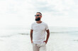 Young bearded hipster guy with beard in white t-shirt and sunglasses at the tropical beach. Mock-up for print. T-shirt template.