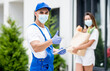 © romaset - Young courier wearing a protective mask and gloves delivers goods to a young woman during quarantine