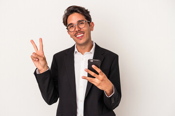 Young mixed race business man holding mobile phone isolated on white background joyful and carefree showing a peace symbol with fingers.