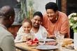 © Seventyfour - Portrait of happy African-American family enjoying dinner together outdoors at terrace, copy space