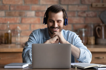 Wall Mural - head shot smiling bearded man in wireless headphones looking at laptop screen, happy student watchin