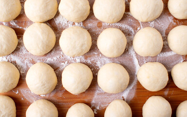 Wall Mural - Yeast dough balls on the wooden board with flour. Preparing to bake buns, pizza or bread. Top view