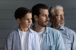 © fizkes - Close up profile three generations of men standing in row on grey studio wall background, looking in distance, serious 7s boy with father and senior grandfather dreaming, visualizing future