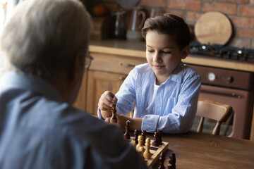 Wall Mural - Little grandson with senior grandfather playing chess at home together close up, family enjoying leisure time, mature grandpa and smart 8s boy engaged in educational activity, logic game on weekend