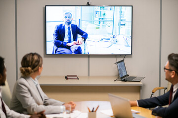 Poster - Intercultural audience looking at mature businessman on display during video conference