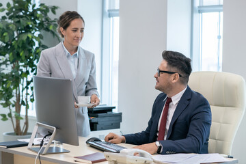 Aufkleber - Busy mature employer looking at his secretary in formalwear carrying him cup of tea