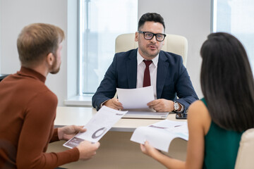 Wall Mural - Confident mature businessman with paper discussing financial points or data with his two subordinates