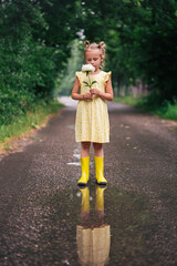 Portrait of girl of 6 years in yellow dress and rainboots standing in the park