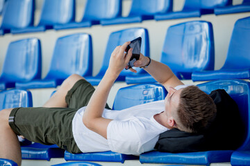 Young teenager with mobile phone lying on chairs on stadium