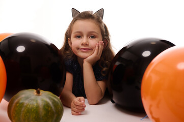 Wall Mural - Traditional event, Halloween party concept. Beautiful little witch girl in hoop with cat ears lying on white background with copy space next to pumpkin and orange black balloons