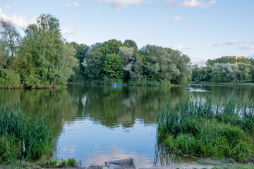 Wall Mural - Panorama of the lake in the city park. Green trees, reeds, dense foliage on the trees. Day Autumn. Russia.